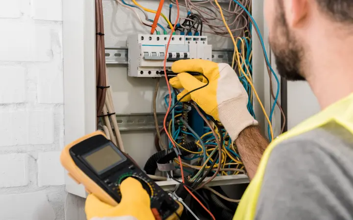 A Mr. Bright Electric electrician holding a telemeter and checking wires in an electrical box
